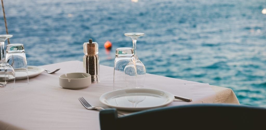 A table set with empty plate and glass, ashtray, and a battle of black pepper.