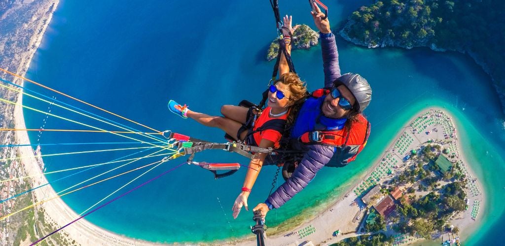 A woman and a man paragliding underneath of them a island of Ölüdeniz. 