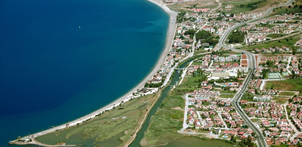 Aerial view of Çalış Beach. A big blue sea and land, building and houses, rivers and street roads. 