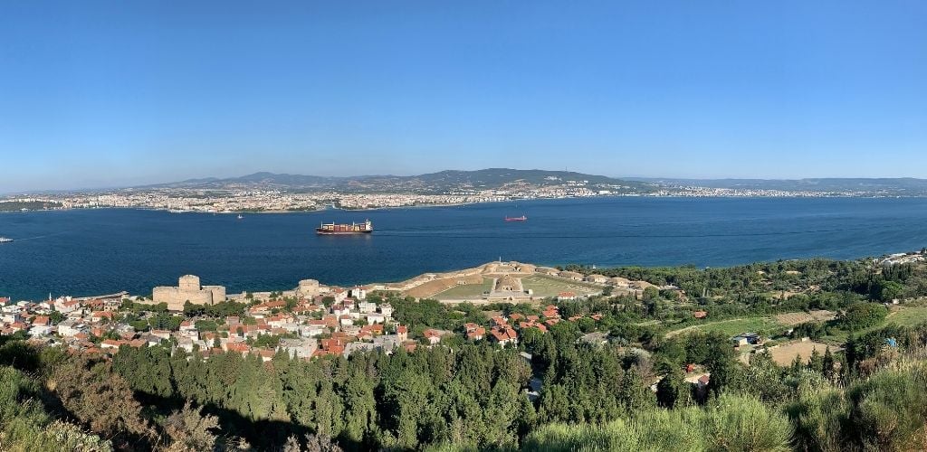 Aerial image of Cankkale and Kilitbahir. In the center, there is a cargo ship and a saltwater. There is also a building structure and trees. 