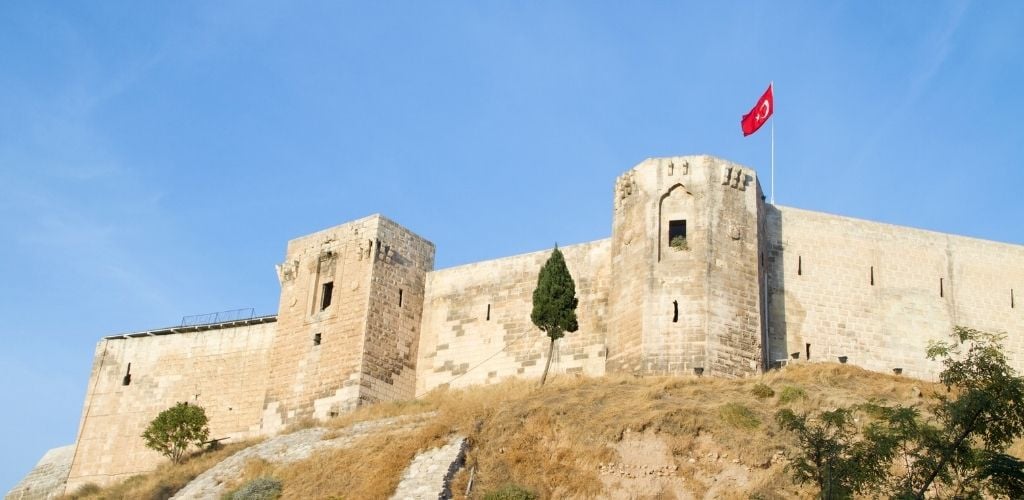 Gaziantep Citadel atop a hill or mountain, and a Turkish flag. 