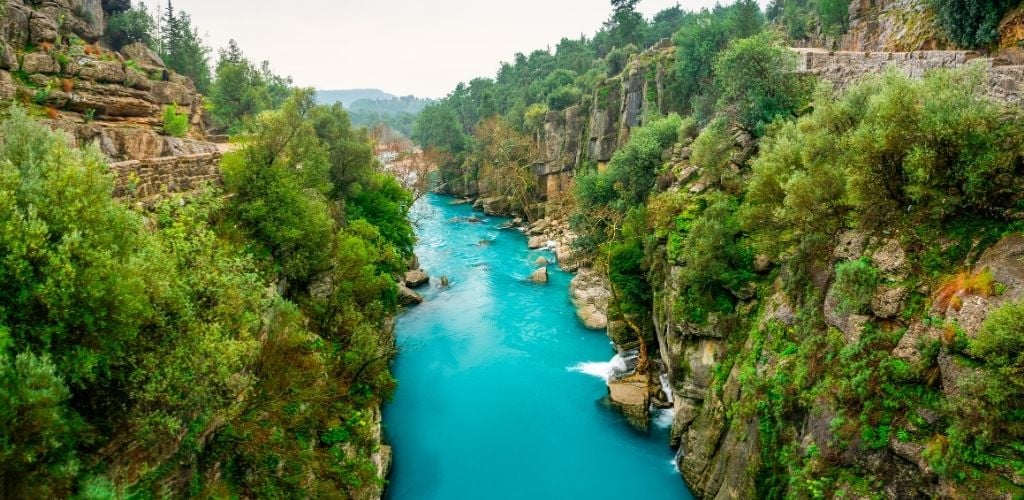 A blue water and stone wall on both sides with some of green trees. 