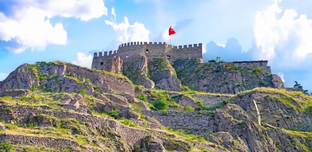 A castle on the top of the hill. and a flag of turkey. 