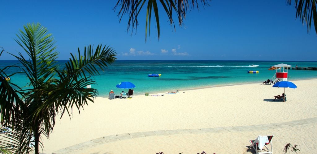 A beach with white sand. Two modest beach tents and four people sunbathing on the beach. 