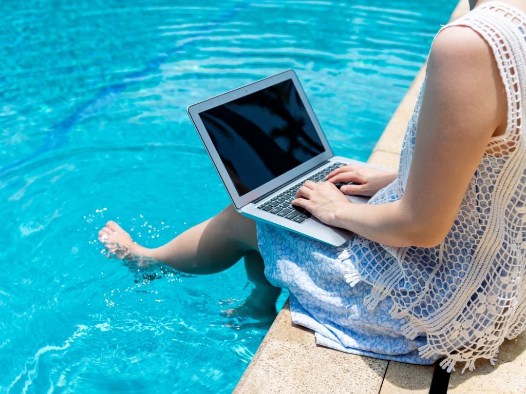 woman working on a laptop with feet in the pool