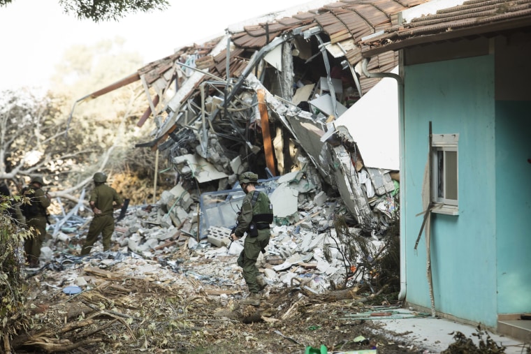 Israeli soldiers walk near houses that were destroyed during a Hamas attack on the kibbutz
