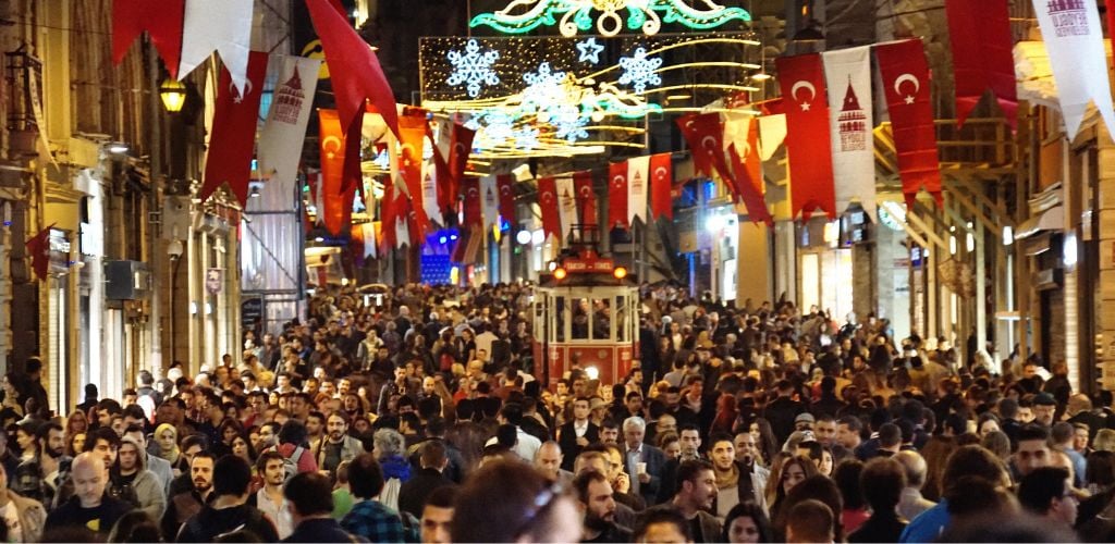 A night crowded people in the middle of the road and a little street operating train in the center. 