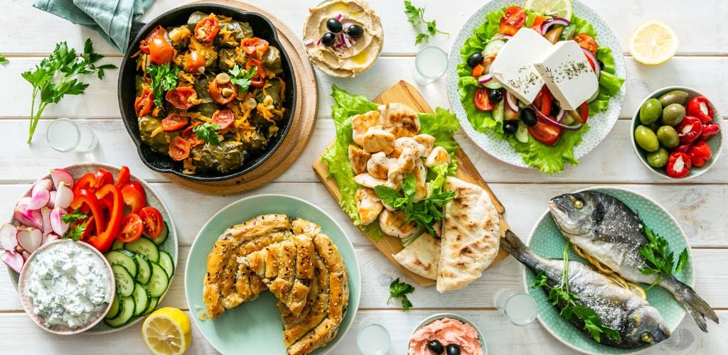 A bunch of different variety of foods. A plate of two fish, pita, bread and vegetables.