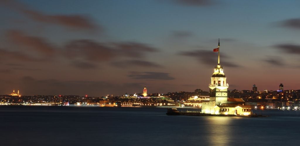 A tower in the lake and city lights in the back ground. 