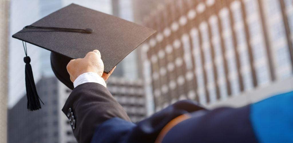 man holding a university gown cap as he graduates