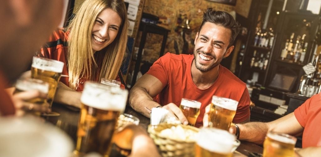A man and a woman laughing and drinking beer with their friends. 