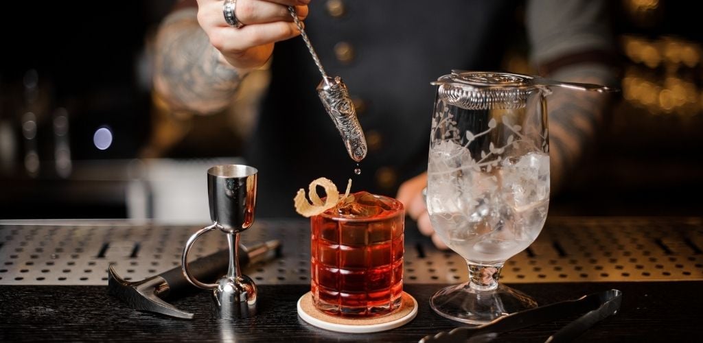 A bartender man with a tattoo on his arm preparing a glass of cocktail drink. 