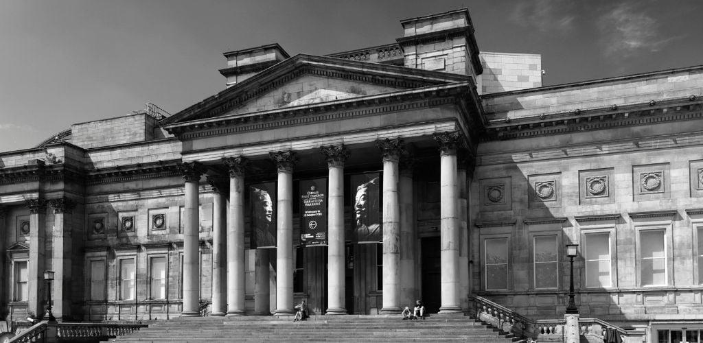 A black-and-white view of the famous World Museum and three individuals sitting on the museum's stairs. 