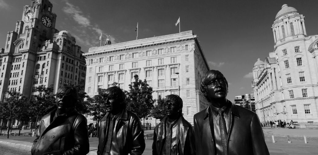 A black and white image of Beatles group statue and building structure at the background. 