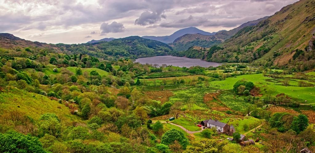 A lake surrounded by a mountain, with one house at the mountain's edge. 