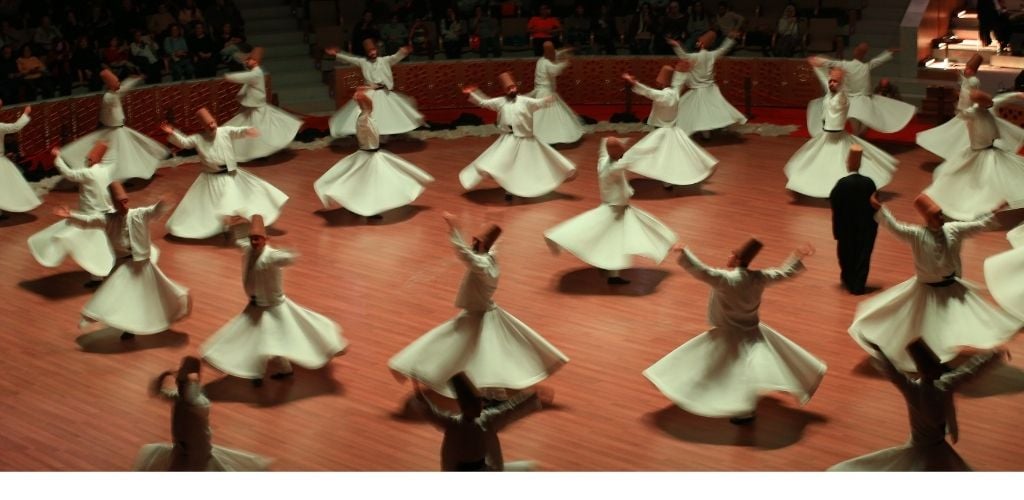 A group of man wearing white skirt and top and doing whirling dervish show.