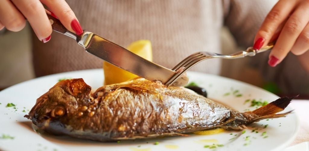 A woman eating one large fish. 