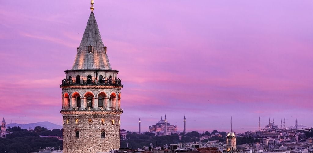 Galata Tower, with purple sky and surrounded by buildings. 