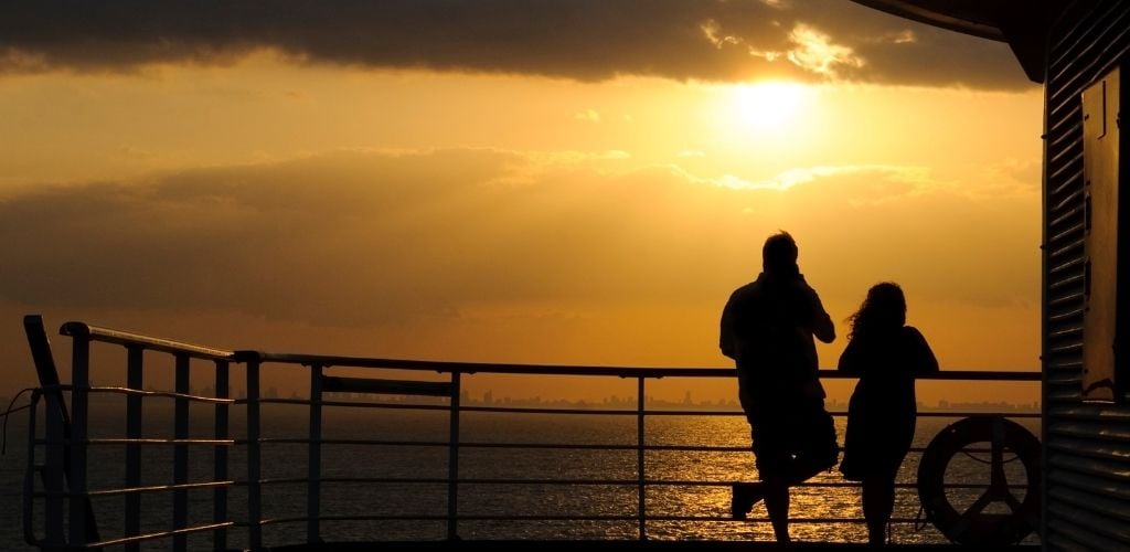 A man and woman standing in the side of cruise with sunset view and sea