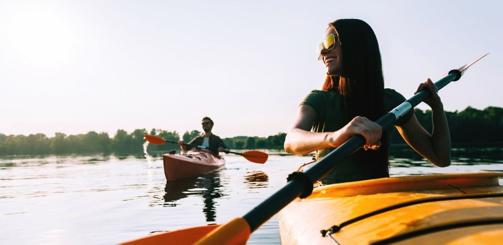 A girl and a man riding on a kayak with lake and trees in day time.