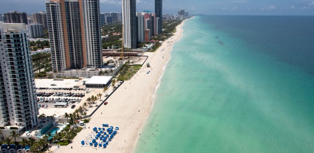 Aerial Miami Beach is building structures near the shore, blue tent, and blue sea. 