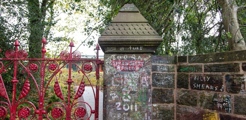 A red gate and post with written "Strawberry Field" and other vandalism.