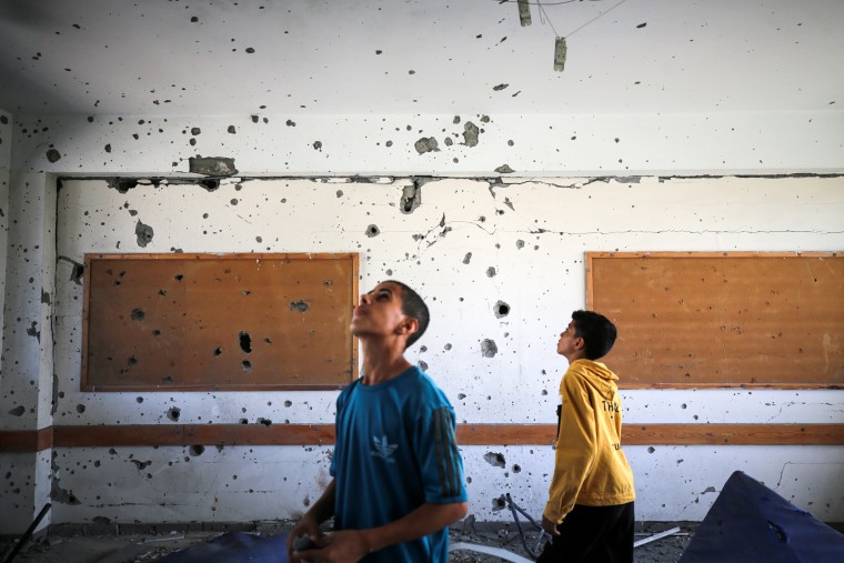 Two young Palestinian boys look up at the walls and ceiling of a room pockmarked with holes in a United Nations-run school being used as a shelter in Al-Maghazi, Gaza.