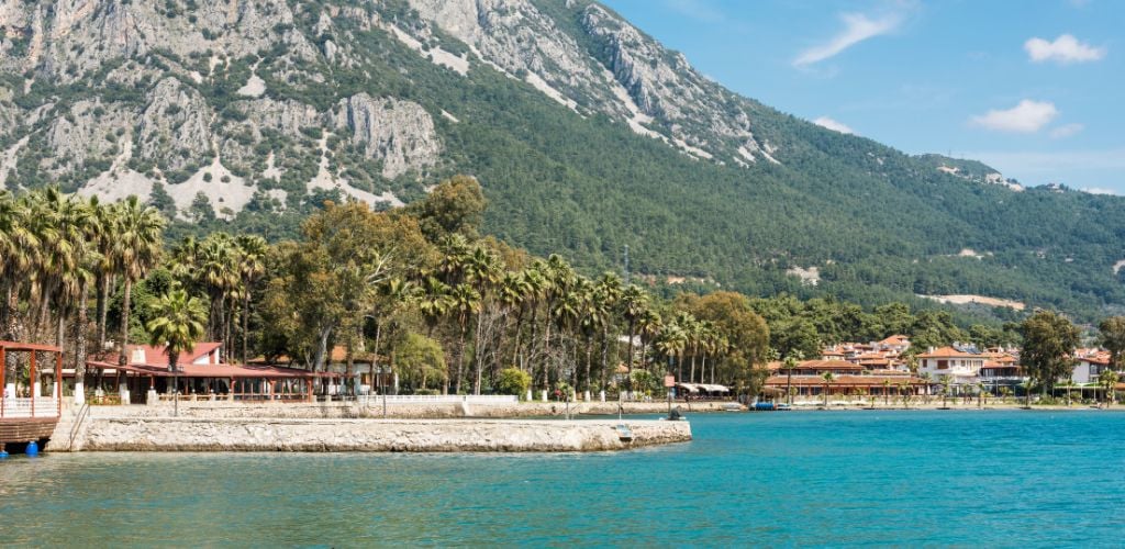 A pier, trees on the side land, a housing structure, and a distant mountain. 