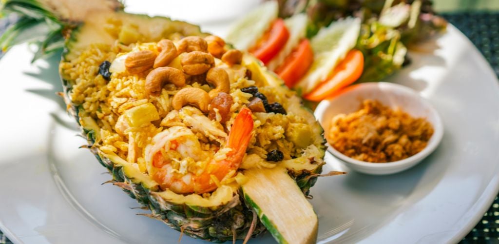Pineapple fried rice with shrimp, beautiful food decoration, serve fried rice in a half fresh pineapple, cashew nuts on top. close-up food image, natural lighting. 