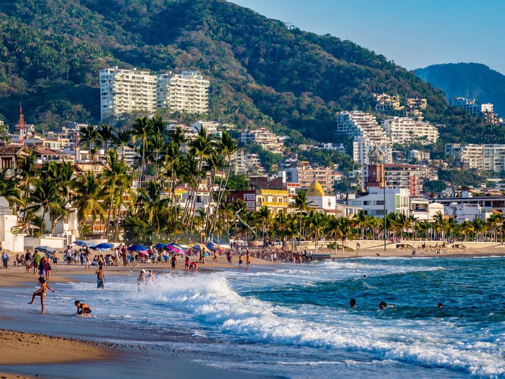 people swimming in the ocean in puerto vallarta with condominiums on the hill and mountains