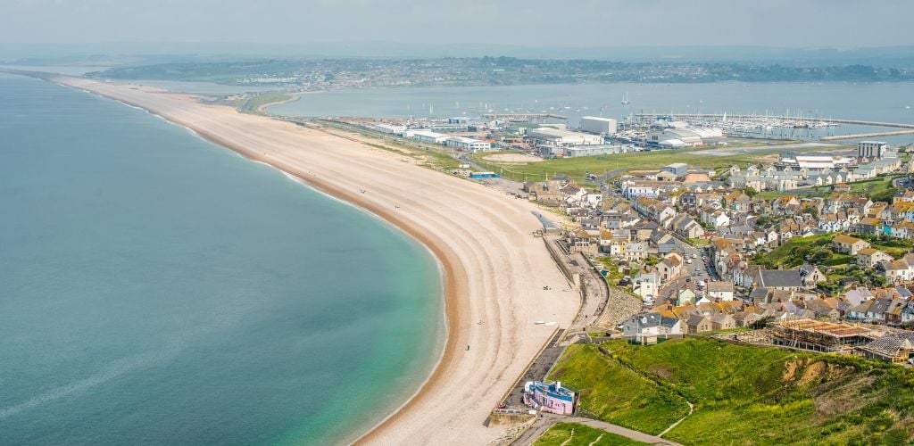 Aerial image of a beach with a calm water and a number of structures near the shore. 