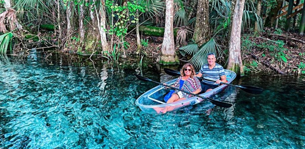 A two-couple kayaking a clear glass kayak on clear blue water.