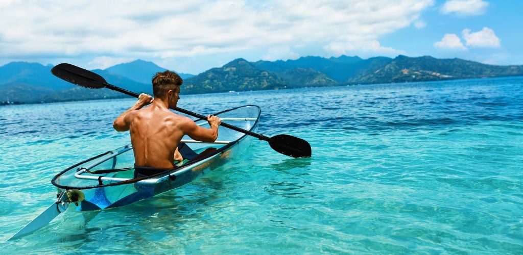 A man kayaking at a lake using a clear kayak paddle.