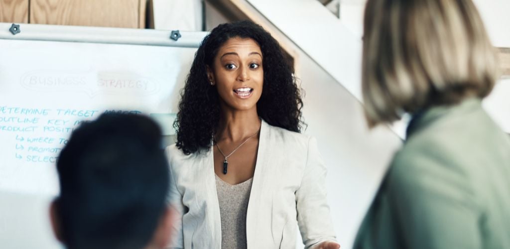 A woman standing in front of a woman and a man, explaining or discus something. 