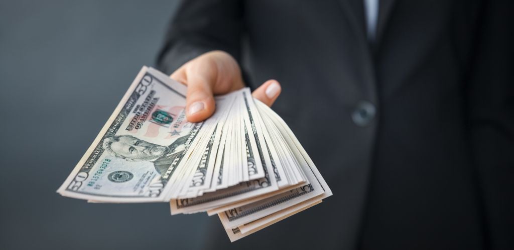 A man in a black suit holding a lot of money. 