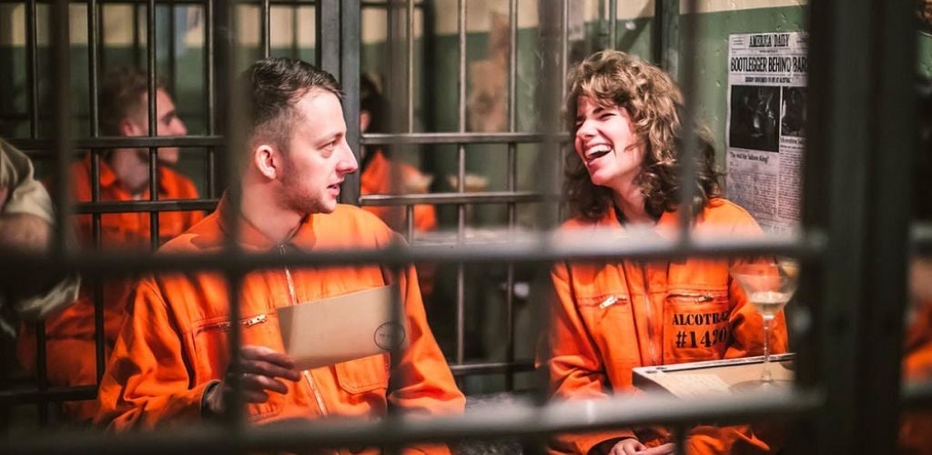 A happy man and a woman wearing a prison uniform inside the prison bars while drinking a cocktail drink. 