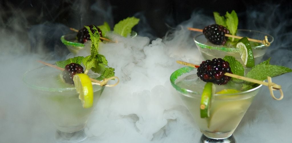 Four Mojito cocktails topped with berries, limes, and mint leaves, as well as nitrogen. 