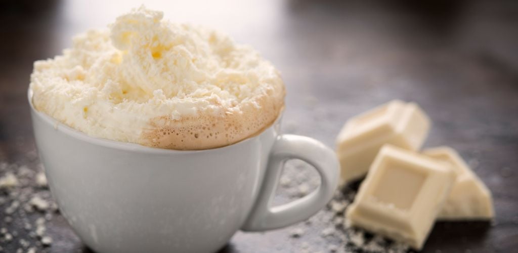 A cup of white chocolate mocha coffee with whipped cream and white chocolate shavings sprinkled over the top. 