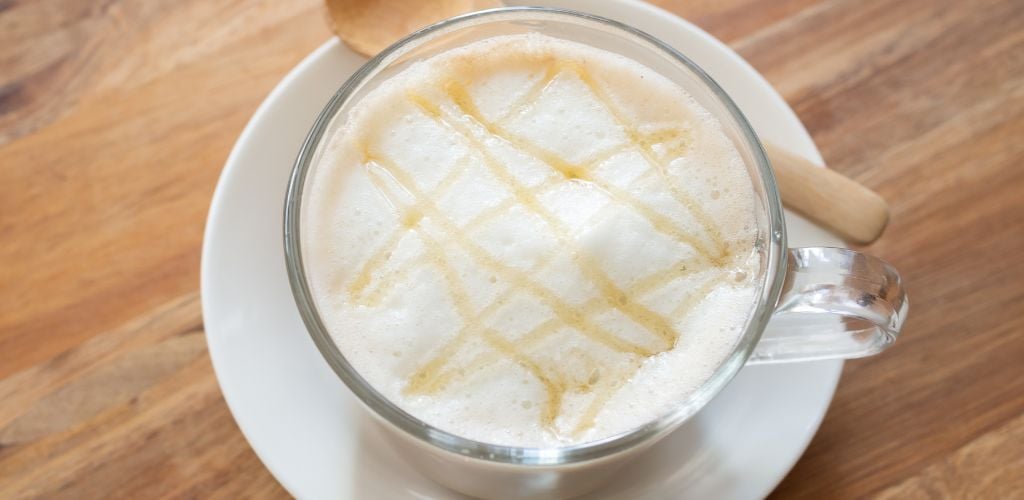 Honey latte in a glass cup and a wood spoon on the side. 