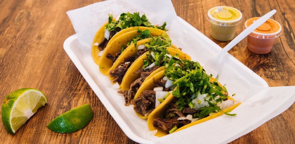 Tacos de Bistec or Mexican Steak Tacos, lime on the side, and two different kinds of sauce. 