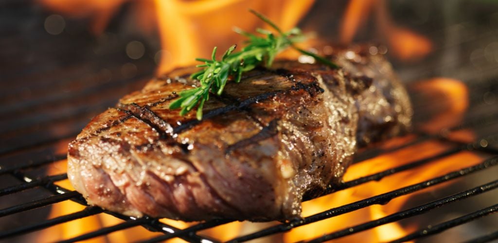 Steak with flame on grill with rosemary