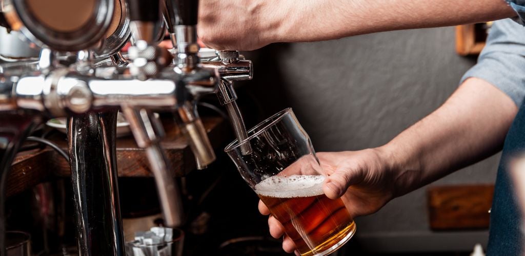 Craft beer from keg. Bartender pours beer in glass from tap