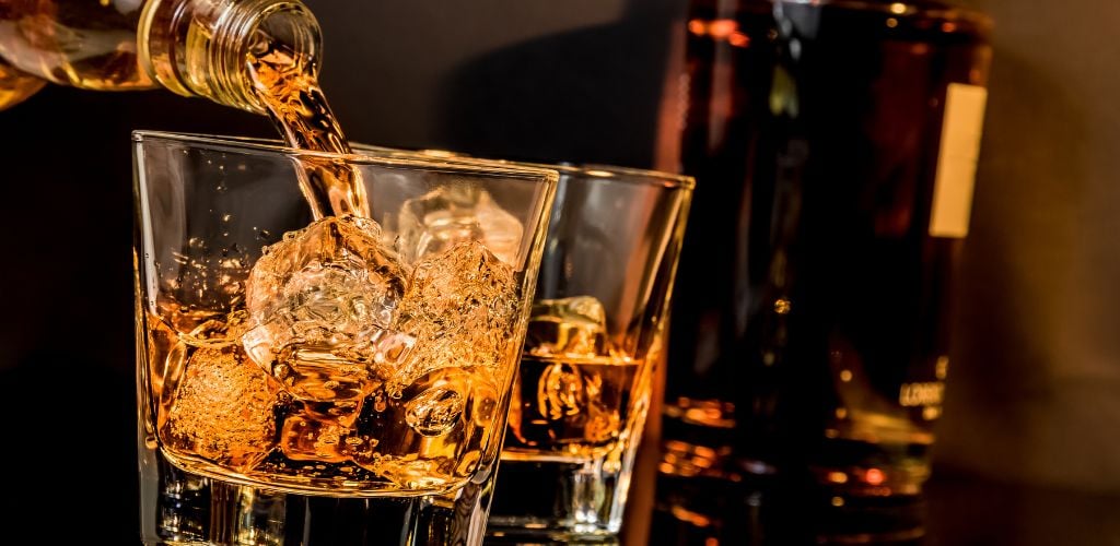 barman pouring whiskey in front of whiskey glass and bottles