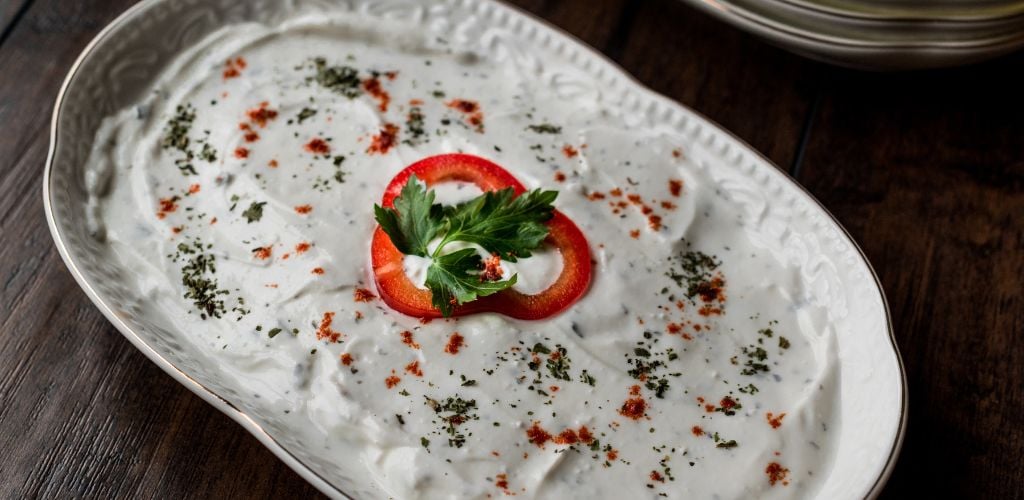 Turkish Appetizer Haydari with yogurt on a white plate on a wooden surface.