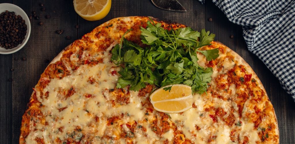 Lahmacun Turkish pizza with melted cheese, fresh parsley, and lemon. 