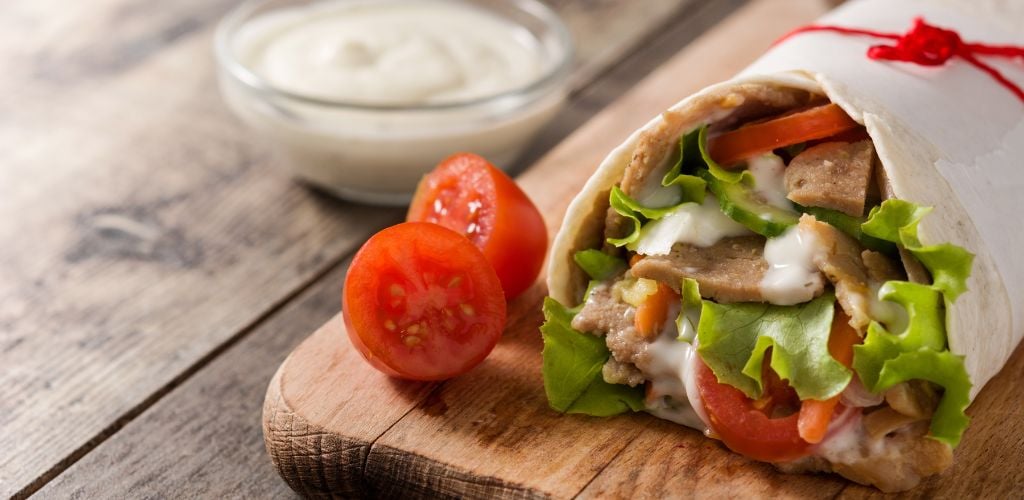 Doner kebab or shawarma sandwich on a wooden table. 