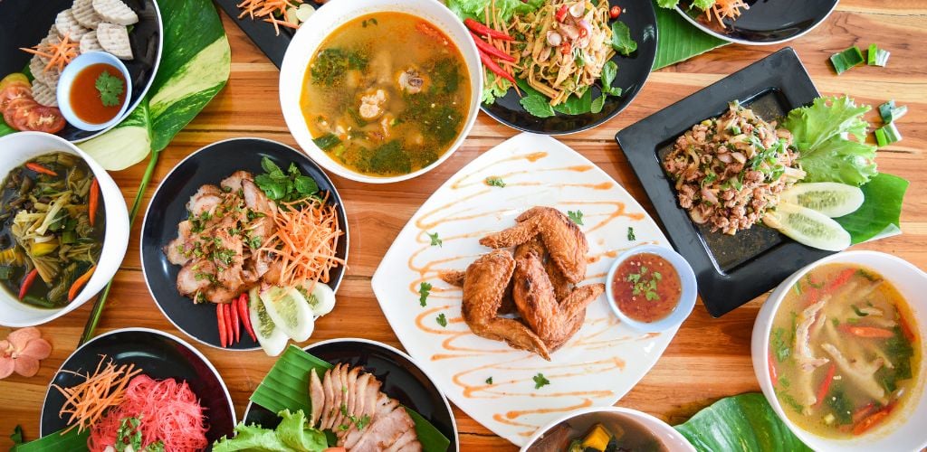 Thai food is served on the dining table. Traditional northeast Isaan is delicious on a plate with fresh vegetables. Many varieties various Thai menu Asian food on a wooden table, top view.