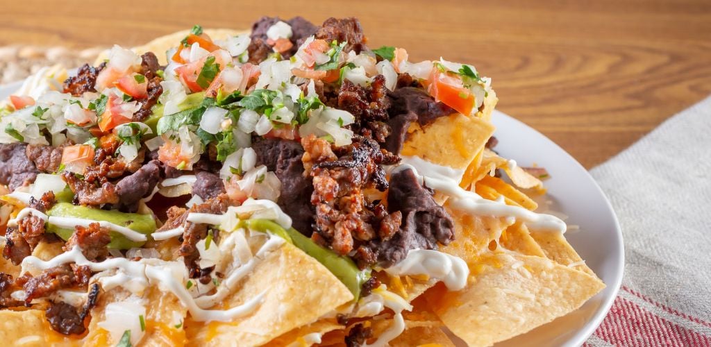 A close-up view of a plate of carne asada nachos in a restaurant or kitchen setting. 