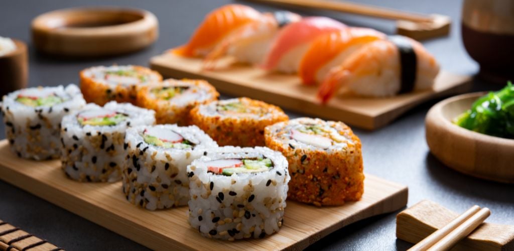 Sushi set uramaki and spicy sushi rolls served on bamboo tray. Various kinds of sushi pieces served on black slate with wooden chopstick. 