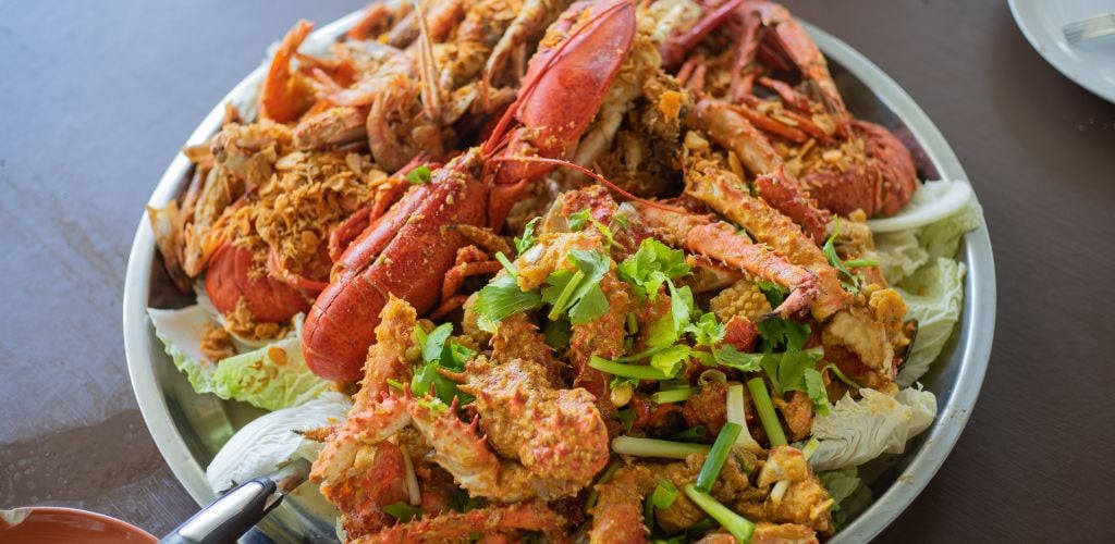 A plate of lobster and crab, and garnished green vegetables. 